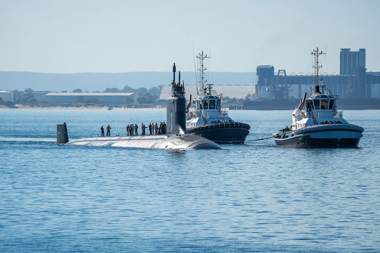 USS Minnesota surfaced and escorted by two tugboats off Rockingham, Western Australia